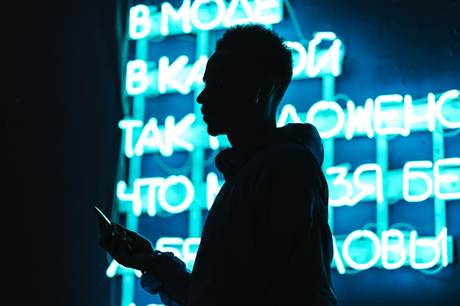 Young man holding phone silhouetted with neon sign in background